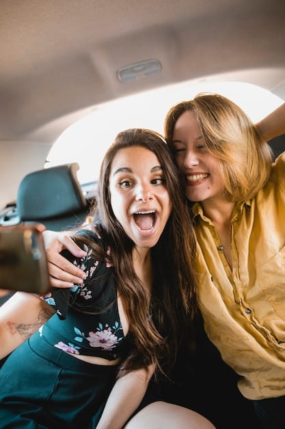A close-up of a mother and daughter in a car, both smiling and holding microphones, as they enthusiastically sing karaoke together. The daughter is wearing headphones, indicating she is listening to the music via a device.