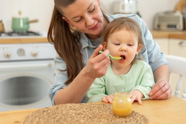 A mom is happily feeding her baby a spoonful of homemade puree. The baby is smiling and looks eager for the next bite. The puree is a vibrant color, suggesting it's made with fresh vegetables.