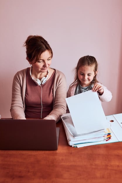 A mother and daughter sitting at a table, using a laptop and a tablet to organize digital photos into folders. They are smiling and appear to be enjoying the task together.