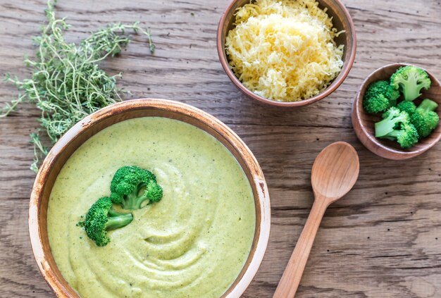 A top-down view of a bowl of bright green pea puree, with a spoon resting beside it. The puree looks smooth and creamy, and the bowl is sitting on a wooden surface.