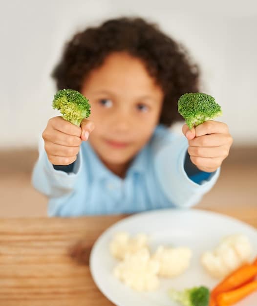 A baby happily reaching for a plate of iron-rich finger foods, such as small pieces of cooked sweet potato, soft tofu cubes, and small broccoli florets.