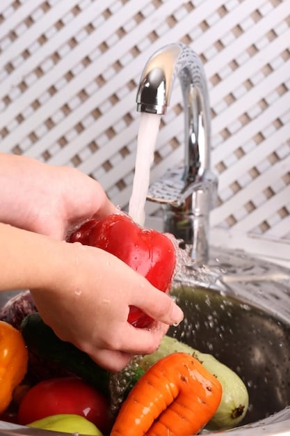 A close-up of a hand carefully washing fruits and vegetables under clean running water in a kitchen sink, highlighting the importance of removing potential pesticide residue.