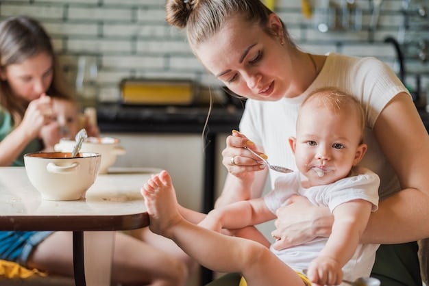A mother is feeding her baby apple puree in a high chair. The baby is looking up at the mother with open mouth, ready to receive the spoon with the puree. The background is blurred to keep the focus on the mother and baby.