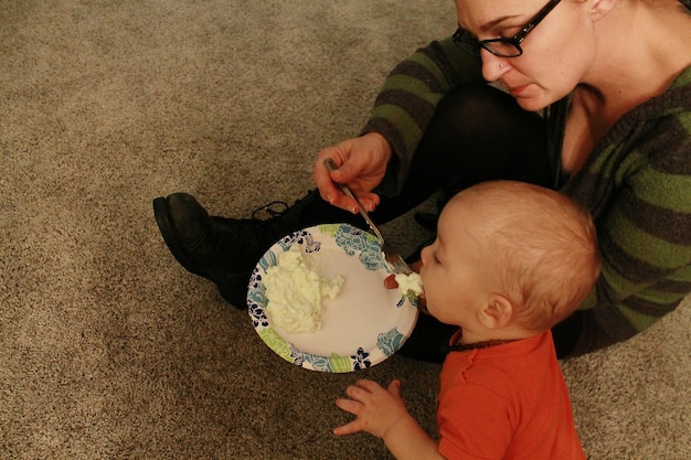 A parent gently offering a spoonful of green pea puree to their baby, who is sitting in a high chair with a bib on. The baby is looking at the spoon with curiosity and anticipation.