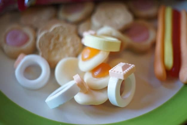A close-up of various foods cut into safe shapes and sizes for baby-led weaning, including steamed carrot sticks, soft apple wedges, and strips of cooked chicken. Emphasis on the correct preparation and presentation of the food.