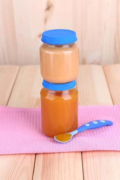 A set of baby food jars or containers with labels for each food item mentioned in the article: pureed meat, iron-fortified cereal, cooked lentils, spinach puree, and prune puree. The scene is well-lit, and the labels are clear and readable, emphasizing the convenience and organization involved in providing iron-rich foods for babies.