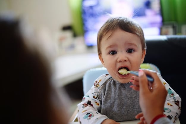 A baby grimacing with a spoonful of green puree near their mouth. The parent looks on patiently.