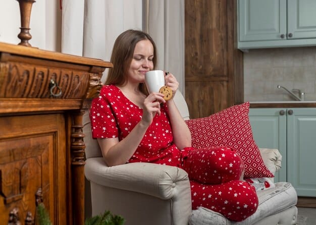 A mother smiling while reading a book in a cozy armchair, with a cup of tea beside her, showcasing a moment of quiet and personal relaxation.