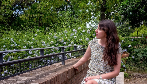 A close-up shot of a mother sitting on a park bench, eyes closed, deeply breathing fresh air, surrounded by green trees and vibrant flowers, conveying peace and rejuvenation.