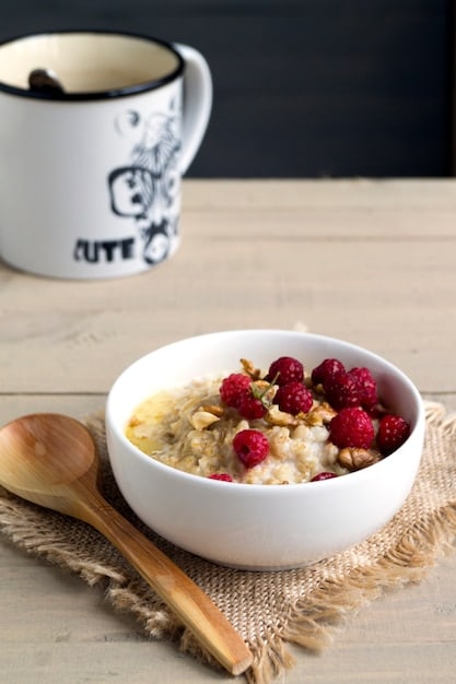 A vibrant image of a breakfast table showcasing a bowl of oatmeal topped with fresh berries, a glass of lemon water, and a small plate of nuts and seeds. The scene is brightly lit, emphasizing the freshness and healthiness of the meal.