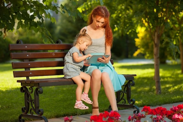 A mother sits on a park bench talking on her phone. She is smiling and relaxed. Her child is playing happily in the park nearby. The park is lush and green.