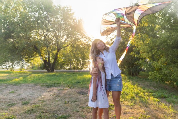 A mother is laughing and playing with her children in a park. They are flying a kite together, and the sun is shining. The image conveys joy and connection.