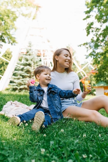 A mom is smiling while playing with her toddler in a park. The sun is shining, and both are laughing. The mom looks relaxed and confident.