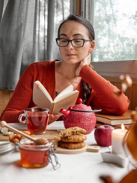 A mother is writing in a journal at her desk. A cup of tea sits beside her, and she looks calm and focused.