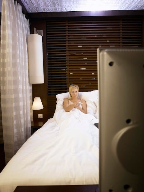 A bedroom interior with blackout curtains, a white noise machine, and earplugs on the nightstand, illustrating a multi-faceted approach to noise reduction.