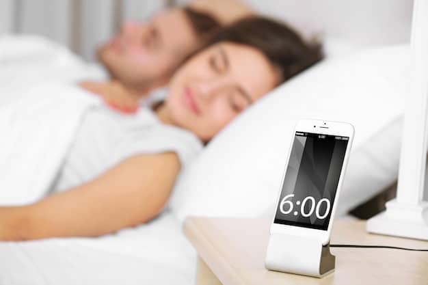 A digital thermostat set to 65 degrees Fahrenheit in a modern bedroom. The room is dimly lit, and a person is seen peacefully sleeping in the bed.